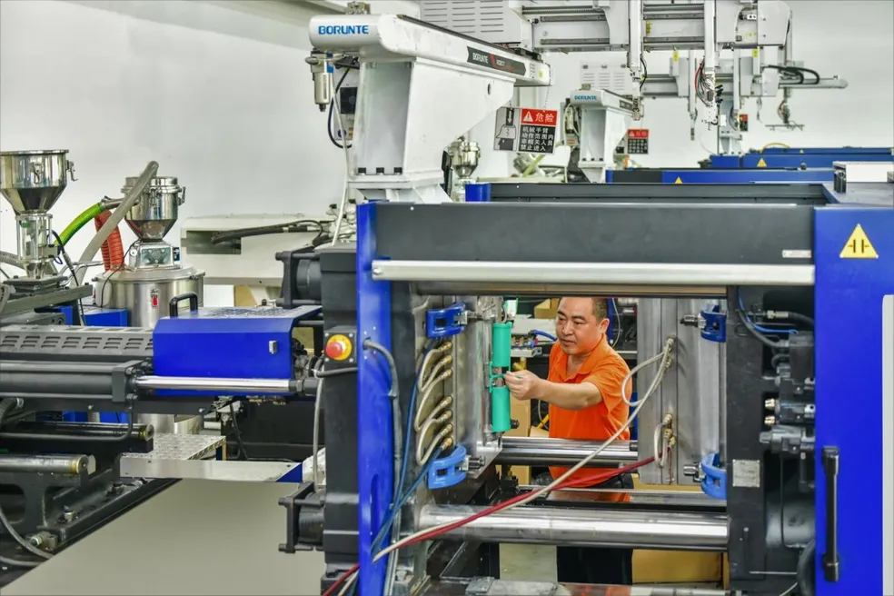 Worker operating injection molding machine in factory